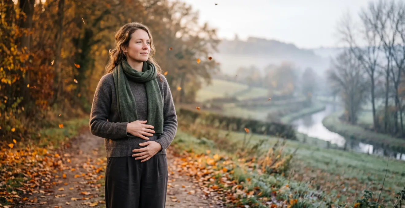 Femme se tenant paisiblement dans un paysage belge en transition entre deux saisons, symbolisant l'harmonie entre cycle menstruel et rythme naturel