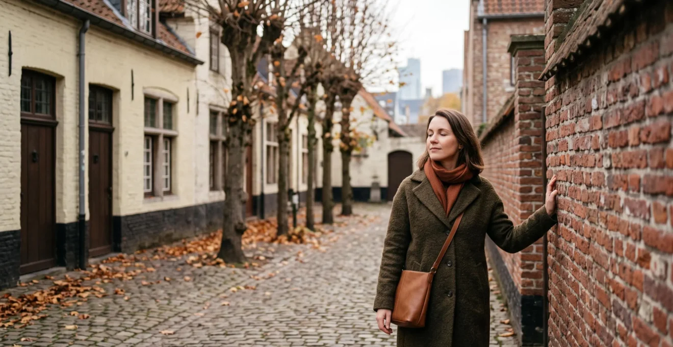 Femme contemplative debout dans une cour tranquille inspirée d'un béguinage belge, en lumière naturelle douce, symbolisant la reconnexion à soi loin du bruit numérique