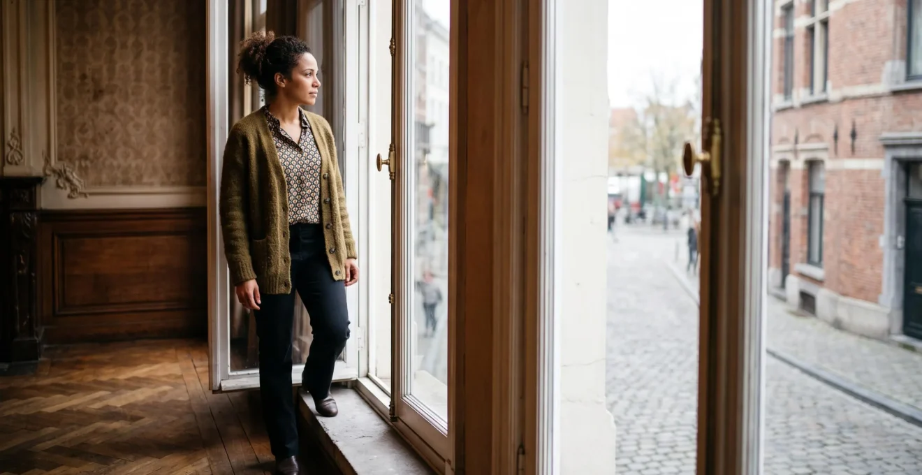 Silhouette d'une femme se tenant dans l'embrasure d'une fenêtre de maison bruxelloise, entre ombre et lumière, symbole de libération
