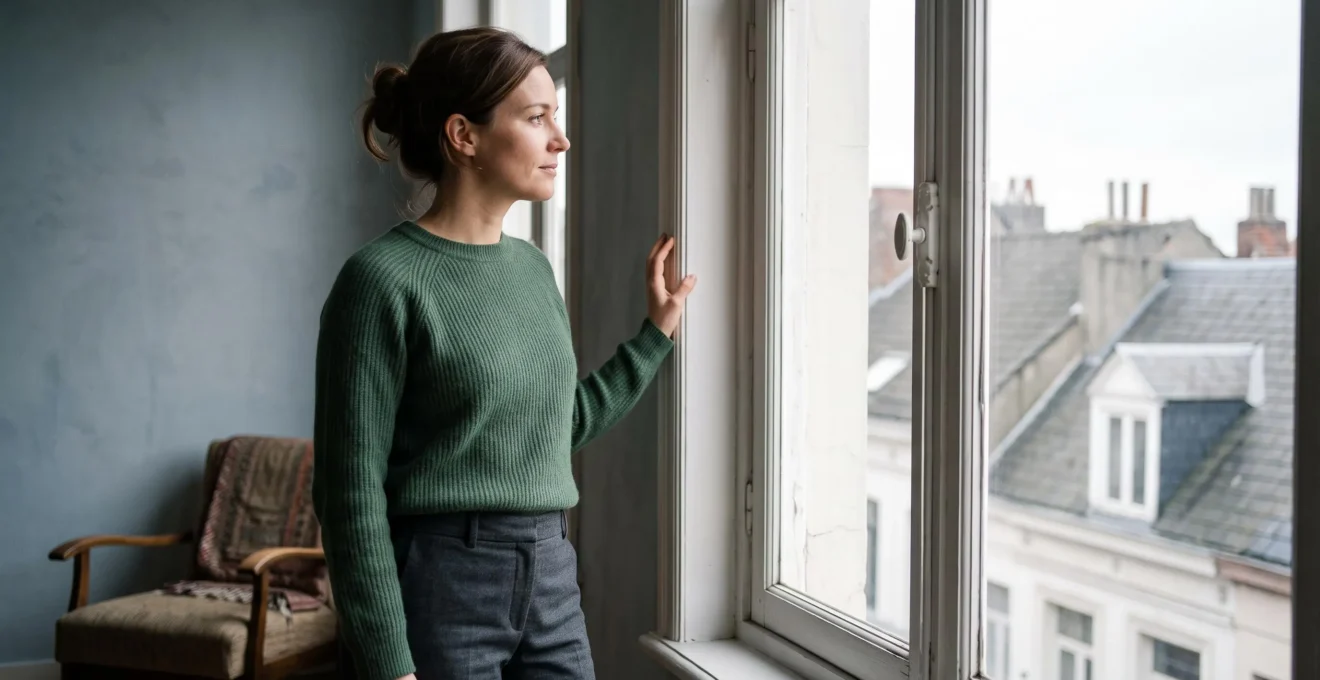 Silhouette d'une femme se tenant pres d'une fenetre d'une maison bruxelloise typique, evoquant le passage de l'ombre vers la lumiere apres une relation d'emprise